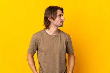 Sarı arka planda izole edilmiş genç yakışıklı adam yan tarafa bakıyor.