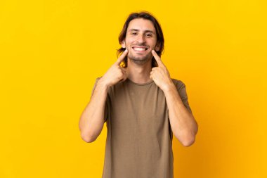 Sarı arka planda izole edilmiş genç yakışıklı mutlu ve hoş bir ifadeyle gülümsüyor.