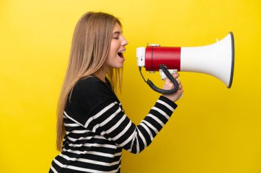 Sarı arka planda izole edilmiş genç beyaz bir kadın megafondan bir şey duyurmak için bağırıyor.