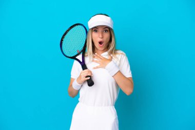 Genç tenisçi Romen kadın mavi arka planda izole edilmiş şaşırmış ve sağa bakarken şok olmuştu