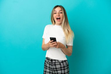 İzole edilmiş mavi arka planı olan genç bir kadın şaşırdı ve bir mesaj gönderiyor.