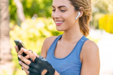 Açık havada giyinen ve telefonlu müzik dinleyen genç sarışın kadın.