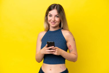 Genç Romen kadın sarı arka planda izole edilmiş cep telefonuyla mesaj gönderiyor
