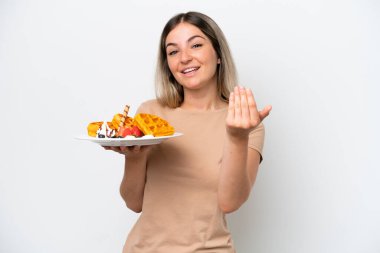 Elinde waffle tutan genç Romen kadın beyaz arka planda izole edilmiş bir şekilde el ele gelmeye davet ediyor. Gelmene sevindim.