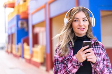 Genç ve güzel Romen kadın açık havada cep telefonu ve düşünceleriyle müzik dinliyor