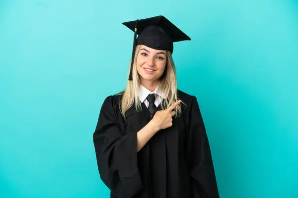Young university graduate over isolated blue background pointing to the side to present a product