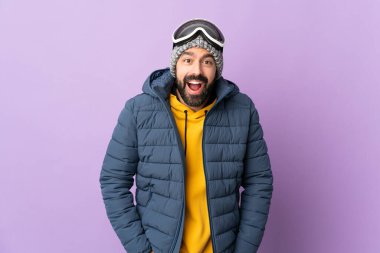 Snowboard gözlüklü kayakçı, yalıtılmış mor arka planda, sürpriz bir yüz ifadesi var.