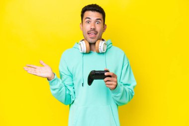 Genç yakışıklı bir adam video oyunu kontrolörüyle oynuyor izole duvarın üzerinde, şok olmuş yüz ifadesiyle.