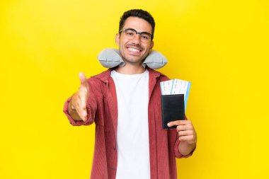 Şişirilebilir Seyahat Yastığı ile genç yakışıklı adam izole edilmiş sarı arka planda iyi bir anlaşma için el sıkışıyor.