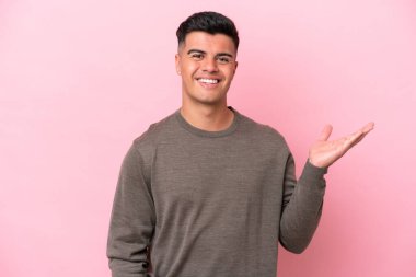 Beyaz tenli yakışıklı, pembe arka planda izole edilmiş. Avucunun içinde hayali bir ilan tutuyor.