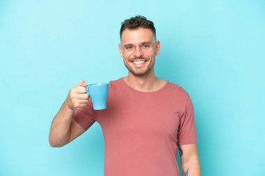 Kafkasyalı genç bir adam elinde kahve fincanı tutarken mavi arka planda izole bir şekilde gülümsüyor.