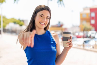Genç, güzel Brezilyalı bir kadın açık havada kahvesini yudumlarken kendine güvenen bir ifadeyle seni işaret ediyor.