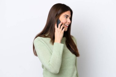 Beyaz arka planda izole edilmiş genç Brezilyalı bir kadın cep telefonuyla sohbet ediyor.