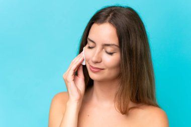 Yüzündeki makyajı silmek için mavi arka planda pamuklu pedi olan beyaz bir kadın.