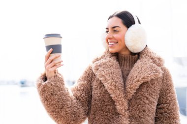 Kış manşeti takan ve elinde kahveyle gezen genç bir kadın.