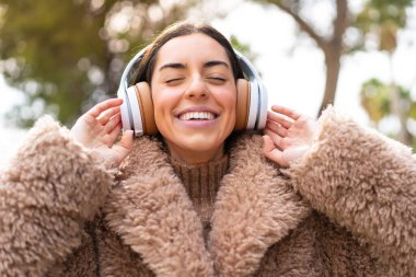 Genç esmer kadın açık havada müzik dinliyor ve şarkı söylüyor.