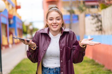 Dışarıda cep telefonu kullanan genç ve güzel bir kız şok olmuş bir yüz ifadesi var.