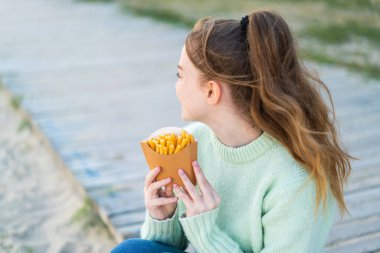 Genç ve güzel bir kız arka tarafta patates kızartması tutuyor.