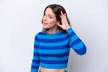 Beyaz arka planda izole edilmiş genç beyaz kadın elini kulağına koyarak bir şeyler dinliyor.