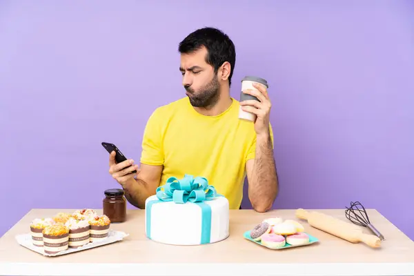 Man in a table with a big cake holding coffee to take away and a mobile