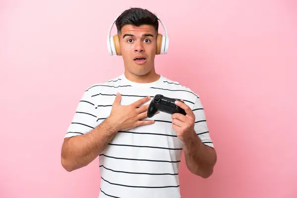 年轻英俊的男子在玩一个粉色背景的视频游戏控制器时 眼睛看着右边 感到惊讶和震惊 — 图库照片