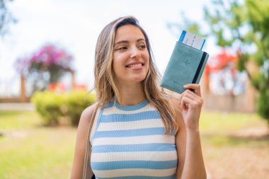 Açık havada elinde mutlu bir ifadeyle pasaport tutan genç ve güzel bir kadın.