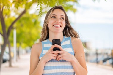 Dışarıda cep telefonu kullanan güzel bir kadın var.