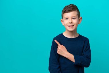 Mavi arka planda izole edilmiş küçük çocuk bir ürünü sunmak için yan tarafı işaret ediyor.