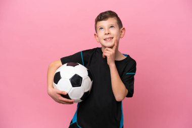 Kafkas futbolcu çocuk pembe arka planda izole edilmiş bir şekilde yukarı bakarken bir fikir düşünüyor.