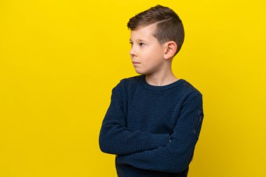 Sarı arka planda izole edilmiş küçük beyaz çocuk kollarını kavuşturuyor.