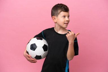 Pembe arka planda izole edilmiş küçük beyaz futbolcu çocuk bir ürünü sunmak için kenarı işaret ediyor.