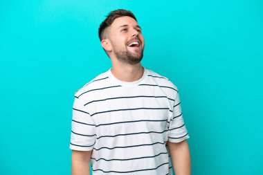 Kafkasyalı genç adam mavi arka planda tek başına gülüyor.