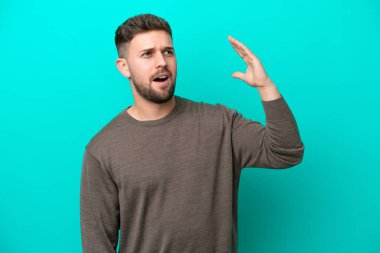 Kafkasyalı genç adam mavi arka planda izole edilmiş, yorgun ve hasta bir ifadeyle.