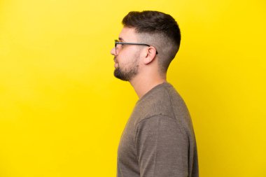 Sarı arka planda gözlüklü, genç, beyaz bir adam.