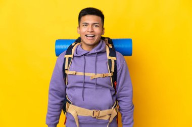 Sarı arka planda büyük bir sırt çantası olan genç dağcı. Şaşırtıcı bir yüz ifadesi var.