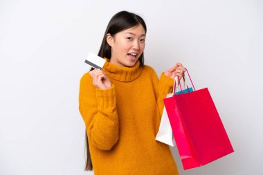 Beyaz arka planda izole edilmiş genç bir Çinli kadın elinde alışveriş çantaları ve bir kredi kartı tutuyor.