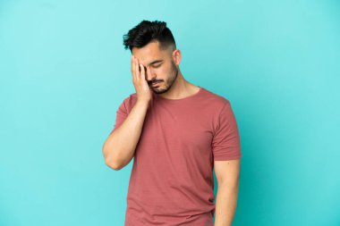 Kafkasyalı genç adam mavi arka planda izole edilmiş, baş ağrısı var.