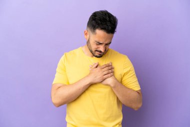 Mor arka planda izole edilmiş genç bir beyaz adamın kalbinde bir ağrı var.