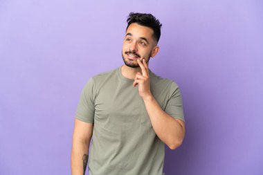 Kafkasyalı genç bir adam mor arka planda izole edilmiş, yukarı bakarken bir fikir düşünüyor.