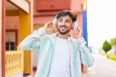 Açık havada müzik dinleyen yakışıklı bir Arap.