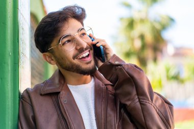 Açık havada yakışıklı bir Arap cep telefonuyla sohbet ediyor.