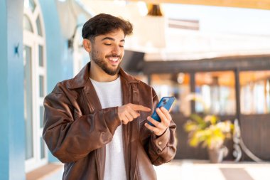 Dışarıdaki yakışıklı Arap cep telefonuyla mesaj ya da e-posta yolluyor.