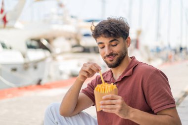 Genç Arap yakışıklı adam açık havada patates kızartması yiyor.