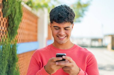 Dışarıdaki İspanyol genç adam cep telefonuyla mesaj yolluyor.