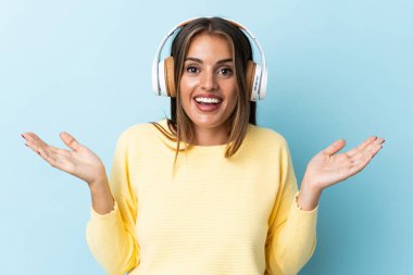Genç Uruguaylı kadın mavi arka planda izole edilmiş şaşırmış ve müzik dinliyor.