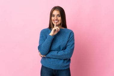 Pembe arka planda izole edilmiş genç Uruguaylı kadın parmağını ağzına koyan sessiz bir jest işareti gösteriyor.