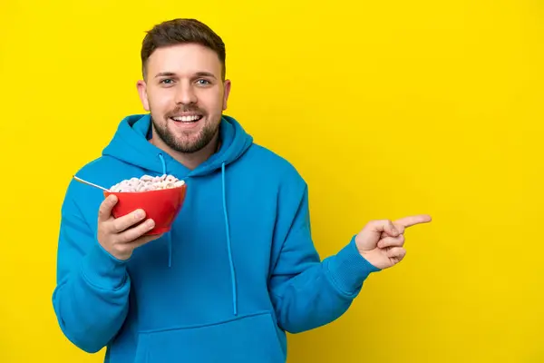 Young Caucasian Man Holding Bowl Cereals Isolated Yellow Background Surprised — Stock Photo, Image