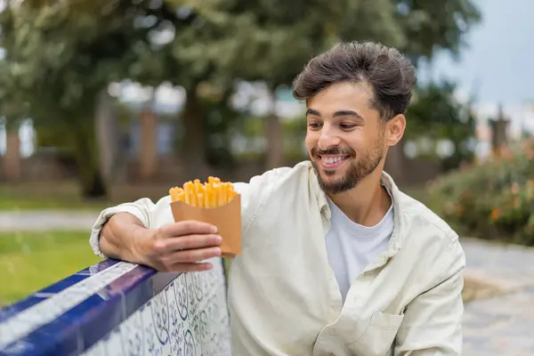 幸せな表情で屋外で揚げチップを保持している若いアラビアのハンサムな男 — ストック写真