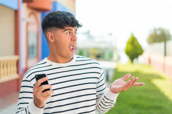 Mladý Hispánec Používající Mobilní Telefon Venku Překvapivým Výrazem Obličeje — Stock fotografie