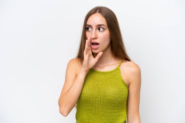 Beyaz arka planda izole edilmiş genç beyaz kadın yan tarafa bakarken sürpriz bir jest yaparak bir şeyler fısıldıyor.